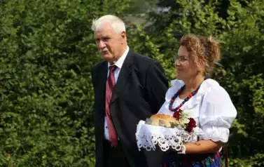 Poch&oacute;d dożynkowy. Korow&oacute;d wielu os&oacute;b ubranych elegancko, a także w stroje ludowe. Kobiety niosą dożynkowe wieńce. Niosą także chleby