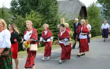 Poch&oacute;d dożynkowy. Korow&oacute;d wielu os&oacute;b ubranych elegancko, a także w stroje ludowe. Kobiety niosą dożynkowe wieńce. Niosą także chleby