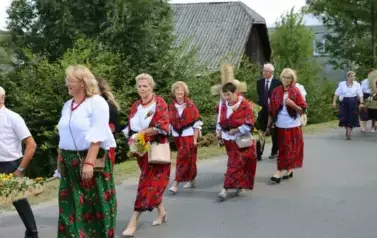 Poch&oacute;d dożynkowy. Korow&oacute;d wielu os&oacute;b ubranych elegancko, a także w stroje ludowe. Kobiety niosą dożynkowe wieńce. Niosą także chleby