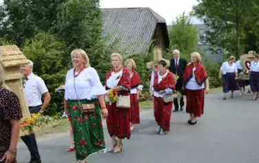 Poch&oacute;d dożynkowy. Korow&oacute;d wielu os&oacute;b ubranych elegancko, a także w stroje ludowe. Kobiety niosą dożynkowe wieńce. Niosą także chleby