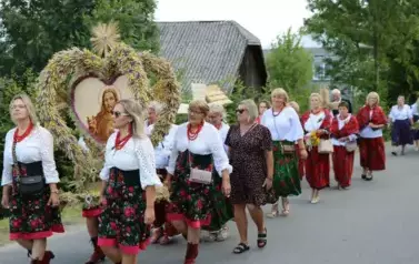 Poch&oacute;d dożynkowy. Korow&oacute;d wielu os&oacute;b ubranych elegancko, a także w stroje ludowe. Kobiety niosą dożynkowe wieńce. Niosą także chleby