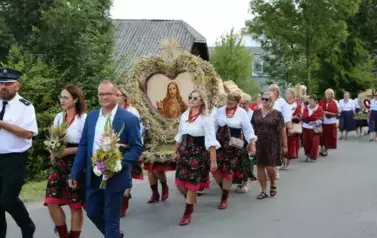 Poch&oacute;d dożynkowy. Korow&oacute;d wielu os&oacute;b ubranych elegancko, a także w stroje ludowe. Kobiety niosą dożynkowe wieńce. Niosą także chleby