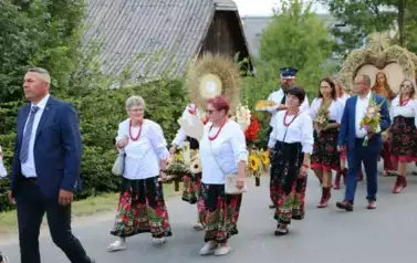 Poch&oacute;d dożynkowy. Korow&oacute;d wielu os&oacute;b ubranych elegancko, a także w stroje ludowe. Kobiety niosą dożynkowe wieńce. Niosą także chleby