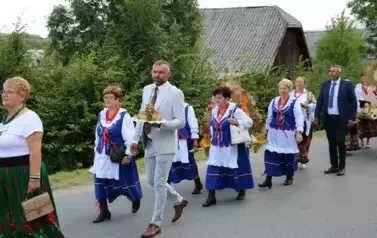 Poch&oacute;d dożynkowy. Korow&oacute;d wielu os&oacute;b ubranych elegancko, a także w stroje ludowe. Kobiety niosą dożynkowe wieńce. Niosą także chleby
