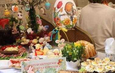 Suto zastawiony st&oacute;ł przykryty białym obrusem, prezentujący wielkanocne wypieki i przekąski.