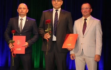 Wyr&oacute;znieni trenerzey w towarzystwie w&oacute;jta. Stoją na scenie podczas wręczania im dyplom&oacute;w oraz r&oacute;ż. 