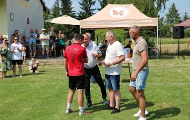 Seria dynamicznych i pozowanych zdjęć z amatorskiego turnieju piłki nożnej, kt&oacute;ry odbył się w pogodny, słoneczny dzień na trawiastym boisku otoczonym brzozami. Zdjęcia przedstawiają pełny przebieg wydarzenia sportowego. Galeria zawiera pozowane fotografie