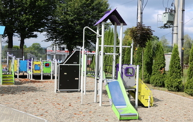 Zdjęcie placu zabaw i zamontowanych element&oacute;w. Na terenie obiektu zamontowano: &bull;	zestaw zabawowo-zręcznościowy &ndash; przystosowany do potrzeb os&oacute;b z niepełnosprawnościami, &bull;	2 karuzele tarczowe z siedziskami, &bull;	piaskownicę, &bull;	4 huśtawki sprężynowe (bujaki jed