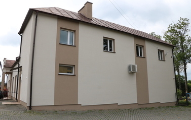 Zestaw 6 zdjęć przedstawia odnowioną elewację budynku Domu Ludowego w Zręcinie po zakończeniu prac remontowych. Budynek posiada nowoczesne wykończenie w jasnej, kremowo-beżowej kolorystyce z ciemniejszymi, beżowo-brązowymi pasami akcentującymi oraz brązow