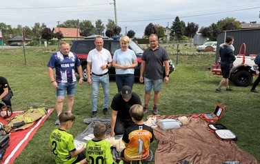 Seria fotografii dokumentujących plenerowe wydarzenie edukacyjne &bdquo;Akademia OLiOC&rdquo;, kt&oacute;re odbyło się na boisku trawiastym w Kopytowej pod patronatem Gminy Chork&oacute;wka. Zdjęcia przedstawiają praktyczne warsztaty z pierwszej pomocy przedmedycznej oraz prezenta