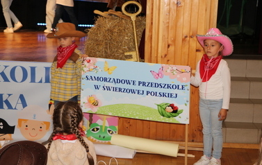 Dwoje dzieci stoi przy scenie i trzyma baner z napisem samorządowe przedszkole w Świerzowej Polskiej. 