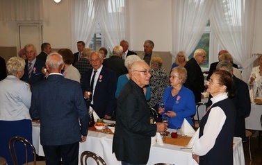 Zdjęcia z uroczystości Złotych God&oacute;w w Domu Ludowym w Zręcinie. Przedstawiają one występy męskiej sekcji Zespołu Śpiewaczego &bdquo;Chorkowianie&rdquo; w tradycyjnych strojach ludowych, oficjalne wystąpienie władz gminy Chork&oacute;wka oraz pamiątkowe kadry z jubilatami odznaczonymi Medalami za Długoletnie Pożycie Małżeńskie.