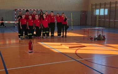 Zdjęcia przedstawiają uczestnik&oacute;w w strojach sportowych i strażackich podczas rywalizacji na hali sportowej, m.in. dynamiczne konkurencje z wężami strażackimi, uroczystą zbi&oacute;rkę wszystkich drużyn, a także momenty wręczania puchar&oacute;w, dyplom&oacute;w oraz nagr&oacute;d indywidualnych przez zaproszonych gości i przedstawicieli straży pożarnej.
