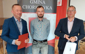 Na zdjęciu nagrodzony Tomasz Wojtowicz,  W&oacute;jt Gminy Chork&oacute;wka oraz zastępca na tle banneru z herbem gminy. 