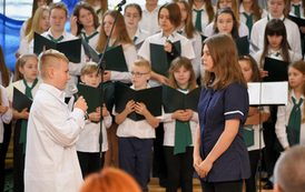Akademia szkolna z okazji Dnia Patrona szkoły. Ch&oacute;r mieszany w biało-czarnych strojach. Dwoje uczni&oacute;w w strojach nawiązujących do czas&oacute;w kiedy żył Ignacy Łukasiewicz. 