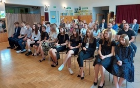 Nagrodzeni uczniowie oraz ich rodzice siedzą na krzesłach w sali gdzie odbywa się uroczystość. 