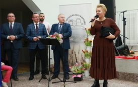 Troje mężczyzn w ciemnych garniturach i kobieta w brązowej syukience. 