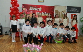 Chłopcy w białych koszulach i kapeluszach, tańczą przy krzesłach.