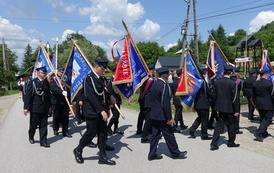 Zdjęcie wykonane podczas przemarszu uczestnik&oacute;w spotkania. Orkiestra Dęta na czele., tuz za nią strażacy w mundurach. Widoczne r&oacute;wnież poczty sztandarowe
