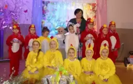 Grupa dzieci bierze udział w przedstawieniu scenicznym. Część dzieci ubrana jest w czerwone stroje kogut&oacute;w z ż&oacute;łtymi dziobami i czerwonymi grzebieniami, a druga część &ndash; w ż&oacute;łte stroje kurczak&oacute;w z czarnymi oczkami i puszystymi ogonkami. Jedno dziecko z gru