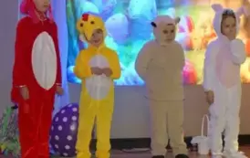Grupa dzieci bierze udział w przedstawieniu scenicznym. Część dzieci ubrana jest w czerwone stroje kogut&oacute;w z ż&oacute;łtymi dziobami i czerwonymi grzebieniami, a druga część &ndash; w ż&oacute;łte stroje kurczak&oacute;w z czarnymi oczkami i puszystymi ogonkami. Jedno dziecko z gru