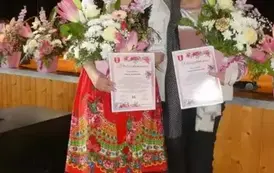 Pani Marysia w stroju ludowym obok niej Pani Teresa trzymają w dłoniach kwiaty. 