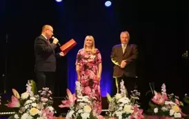 Trzy osoby W&oacute;jt Dyrektor Małgorzata Wierdak oraz dołaczył Bogusław pacek. to wręczenie podziękowań dla nich, na scenie pełnej kwiat&oacute;w. 
