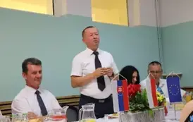Przy stole siedzą osoby, głowny kadr prezentuje dw&oacute;ch meżczyzn w białych koszulach. 