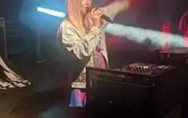 na scenie kobieta DJ Olga. Kolorowe świtała oraz sprzęt do prowadzenia imprezy tanecznej. 