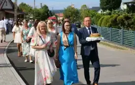Poch&oacute;d dożynkowy. Korow&oacute;d wielu os&oacute;b ubranych elegancko, a także w stroje ludowe. Kobiety niosą dożynkowe wieńce. Niosą także chleby