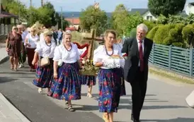 Poch&oacute;d dożynkowy. Korow&oacute;d wielu os&oacute;b ubranych elegancko, a także w stroje ludowe. Kobiety niosą dożynkowe wieńce. Niosą także chleby