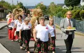 Poch&oacute;d dożynkowy. Korow&oacute;d wielu os&oacute;b ubranych elegancko, a także w stroje ludowe. Kobiety niosą dożynkowe wieńce. Niosą także chleby