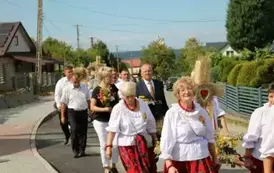 Poch&oacute;d dożynkowy. Korow&oacute;d wielu os&oacute;b ubranych elegancko, a także w stroje ludowe. Kobiety niosą dożynkowe wieńce. Niosą także chleby