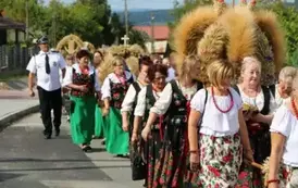 Poch&oacute;d dożynkowy. Korow&oacute;d wielu os&oacute;b ubranych elegancko, a także w stroje ludowe. Kobiety niosą dożynkowe wieńce. Niosą także chleby