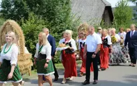 Poch&oacute;d dożynkowy. Korow&oacute;d wielu os&oacute;b ubranych elegancko, a także w stroje ludowe. Kobiety niosą dożynkowe wieńce. Niosą także chleby