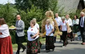 Poch&oacute;d dożynkowy. Korow&oacute;d wielu os&oacute;b ubranych elegancko, a także w stroje ludowe. Kobiety niosą dożynkowe wieńce. Niosą także chleby