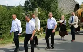 Poch&oacute;d dożynkowy. Korow&oacute;d wielu os&oacute;b ubranych elegancko, a także w stroje ludowe. Kobiety niosą dożynkowe wieńce. Niosą także chleby