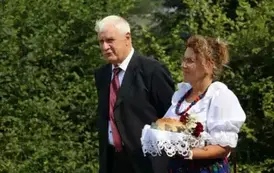 Poch&oacute;d dożynkowy. Korow&oacute;d wielu os&oacute;b ubranych elegancko, a także w stroje ludowe. Kobiety niosą dożynkowe wieńce. Niosą także chleby