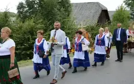 Poch&oacute;d dożynkowy. Korow&oacute;d wielu os&oacute;b ubranych elegancko, a także w stroje ludowe. Kobiety niosą dożynkowe wieńce. Niosą także chleby