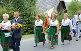 Poch&oacute;d dożynkowy. Korow&oacute;d wielu os&oacute;b ubranych elegancko, a także w stroje ludowe. Kobiety niosą dożynkowe wieńce. Niosą także chleby
