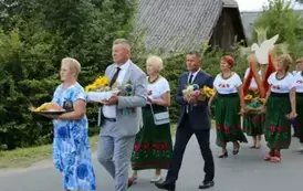 Poch&oacute;d dożynkowy. Korow&oacute;d wielu os&oacute;b ubranych elegancko, a także w stroje ludowe. Kobiety niosą dożynkowe wieńce. Niosą także chleby.   