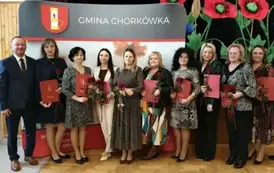 Nagrodzeni nauczyciele, pozują na tle ścianki z herbem gminy. 