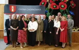 Nagrodzeni nauczyciele, pozują na tle ścianki z herbem gminy. 