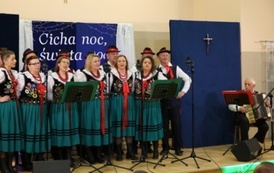 Zesp&oacute;ł ludowy Chorkowianie, w strojach stylizowanych na ludowe śpiewają na scenie, zar&oacute;wno kobiety jak i mężczyźni. 