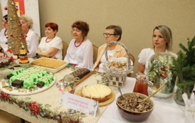Kobiety w białych bluzkach siedzą za stołem na kt&oacute;rym stoją przygotowane potrawy. 