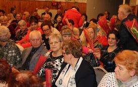 Widok z g&oacute;ry na wypełnioną po brzegi salę widowiskową. Publiczność, składająca się gł&oacute;wnie z kobiet, siedzi w rzędach na szarych krzesłach, uważnie obserwując scenę. Wnętrze ma drewniane panele na ścianach i parkietową podłogę.