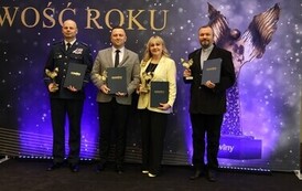 R&oacute;żnorodność i jedność w działaniu na rzecz dobra wsp&oacute;lnego: Małgorzata Wierdak stoi na tle ścianki obok innych laureat&oacute;w, w tym funkcjonariusza policji w galowym mundurze, mężczyzny w garniturze i księdza. Wszyscy trzymają trofea, co symbolizuje, że wyr&oacute;