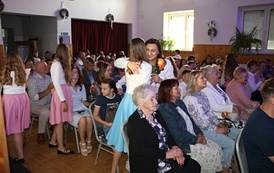Publiczność zgromadzona w sali widowiskowej podczas lokalnego wydarzenia kulturalnego. Widzowie w r&oacute;żnym wieku siedzą na krzesłach, uważnie oglądając program artystyczny. W pierwszym rzędzie widoczne są zaproszone pary oraz przedstawiciele lokalnych władz