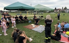 Seria fotografii dokumentujących plenerowe wydarzenie edukacyjne &bdquo;Akademia OLiOC&rdquo;, kt&oacute;re odbyło się na boisku trawiastym w Kopytowej pod patronatem Gminy Chork&oacute;wka. Zdjęcia przedstawiają praktyczne warsztaty z pierwszej pomocy przedmedycznej oraz prezenta