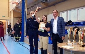 Zdjęcia przedstawiają uczestnik&oacute;w w strojach sportowych i strażackich podczas rywalizacji na hali sportowej, m.in. dynamiczne konkurencje z wężami strażackimi, uroczystą zbi&oacute;rkę wszystkich drużyn, a także momenty wręczania puchar&oacute;w, dyplom&oacute;w oraz nagr&oacute;d indywidualnych przez zaproszonych gości i przedstawicieli straży pożarnej.